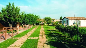A pathway leading to a white building with a tiled roof, surrounded by greenery and trees. - Aranceto Turismo Rurale (Syracuse)