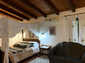 A bedroom with a canopy bed, a sofa, a bedside table, and a wall-mounted air conditioner. - Aranceto Turismo Rurale (Syracuse)