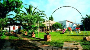 A garden with a paved walkway, palm trees, and a playground with a slide and swings. - Aranceto Turismo Rurale (Syracuse)