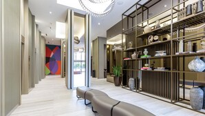 Un moderno vestíbulo de hotel con un largo banco, una estantería con objetos decorativos y una pared abstracta y colorida.
