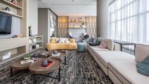 Una sala de estar moderna con un sofá, sillones, una mesita de centro y un televisor. Hay estanterías y adornos en las paredes.