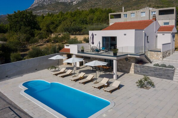 Una villa moderna con piscina, mobiliario exterior y vistas del paisaje circundante.