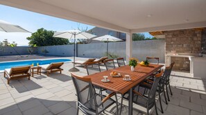 Un patio con piscina, mobiliario de madera y una chimenea de piedra.