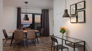 Een moderne eetruimte met een houten tafel en stoelen, een glazen salontafel en uitzicht op de ondergaande zon door grote ramen.