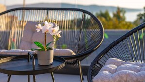 Een balkon met twee zwarte rieten stoelen, een klein rond tafeltje en een potorkidee.