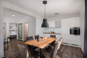 A modern kitchen with white cabinets, a wooden dining table, and a black pendant light.