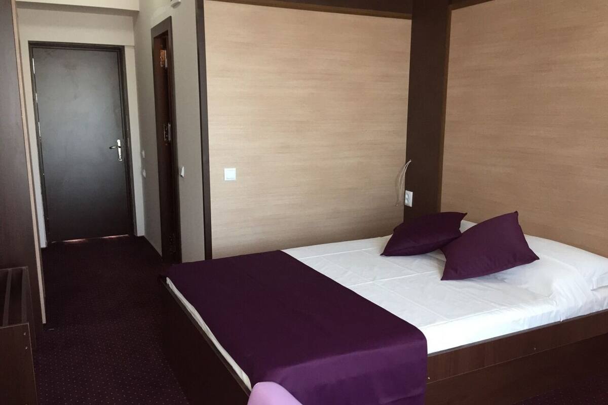 Ein Hotelzimmer mit einem Einzelbett, einer dunklen Tür und Teppichboden.