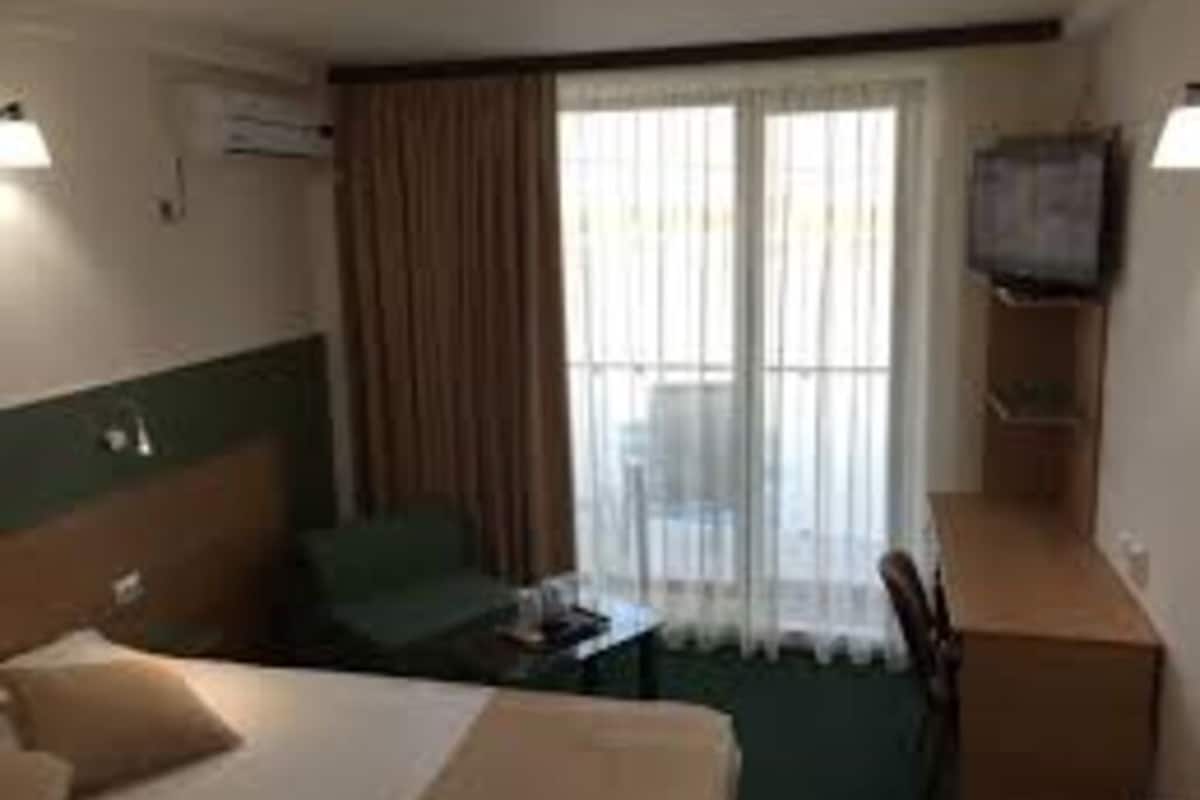 Ein Hotelzimmer mit einem Bett, einem Schreibtisch, einem Stuhl, einem Fernseher und einem Vorhangfenster.