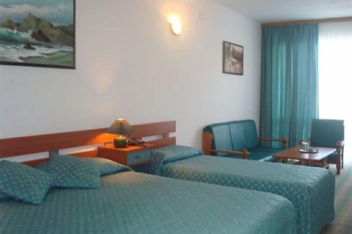Ein Hotelzimmer mit zwei Betten, einem Schreibtisch, einem Sessel, einer Lampe und einem Bild an der Wand.