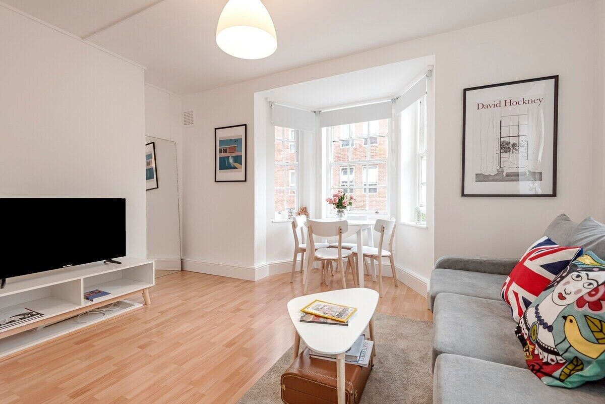 Een moderne woonkamer met een flatscreen televisie, een witte salontafel, een grijze bank en een raam met uitzicht op gebouwen.