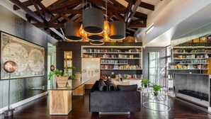 Una sala moderna con un sofá oscuro, una mesa de centro de madera y una estantería llena de libros. Hay un mapa grande en la pared y una chimenea con revestimiento de piedra.