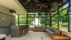 Una cocina moderna con una isla integrada, zona de estar con cojines y ventanas amplias que dan a zonas verdes.