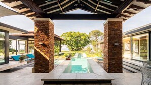 Un área de piscina al aire libre con pilares de piedra, sillones de descanso y un porche cubierto.