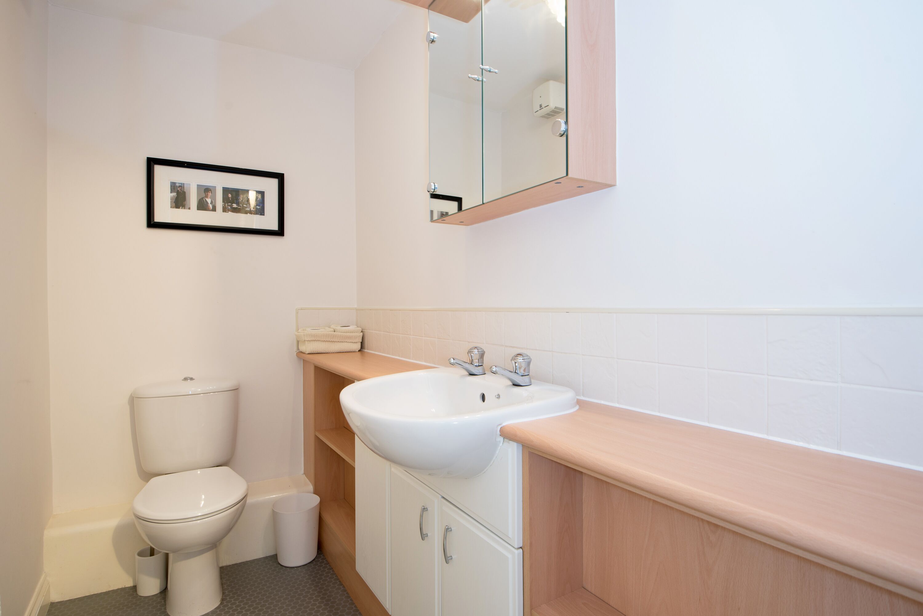 A bathroom with a toilet, sink, mirror, and framed pictures on the wall.