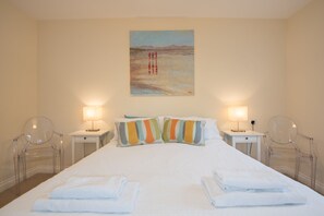 A hotel room with a large bed, two bedside tables, two lamps, and two clear plastic chairs.