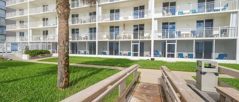 A multi-story hotel with balconies, a palm tree, and a wooden boardwalk.