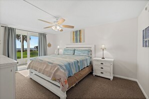 A bedroom with a bed, a nightstand, a dresser, a ceiling fan, and a view of the outdoors. - Oceanfront 2BR Condo Steps to Beach Heated Pool Sleeps 6, Unit 104 (Indian Harbour Beach)