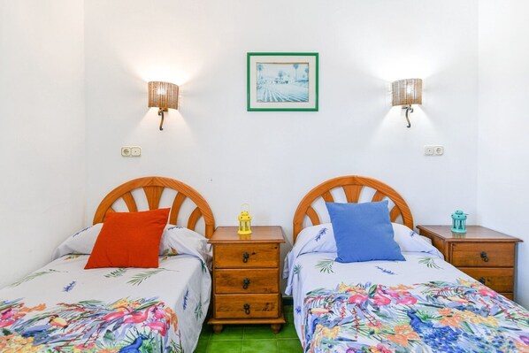 Habitación doble con dos camas de madera, cada una con una mesita de noche. Hay lámparas de pared a cada lado de un cuadro enmarcado.