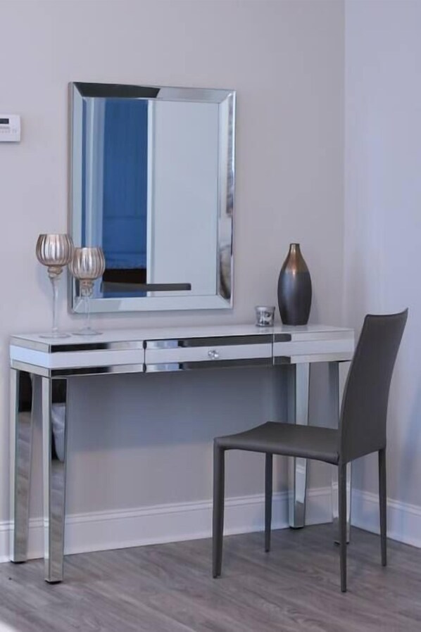 Una habitación moderna con un escritorio blanco, una silla, un espejo grande y un florero sobre el escritorio.