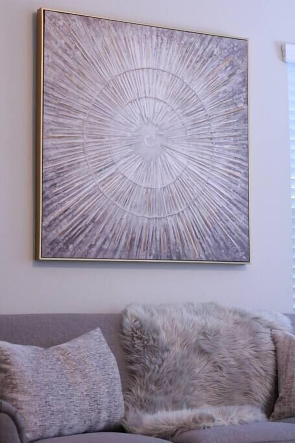 A framed abstract artwork on a wall above a grey sofa with a fluffy throw pillow.