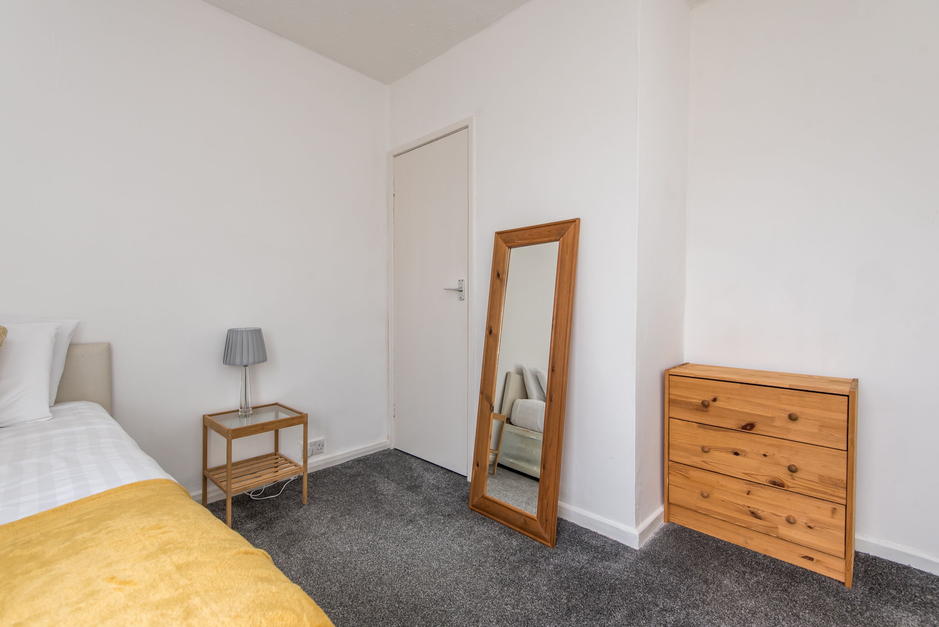 A bedroom with a bed, a bedside table with a lamp, a dresser, and a mirror.