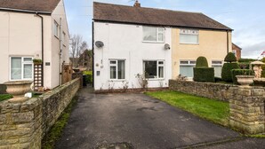 A residential street with two houses, one white and one beige, with a paved driveway and a stone wall. - Broome Road (Durham)