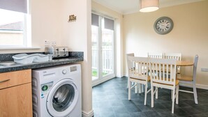A laundry area with a washing machine, a dining table with chairs, and a clock on the wall. - Hillbrook (Stockton-on-Tees)