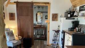 A cozy, rustic interior with a wooden ceiling, a dining area with a wooden table and chairs, a kitchen with a coffee machine, and a living area with a sofa and a lamp. - Cedar Twig Cabin: Serene and cozy (Mt. Juliet)