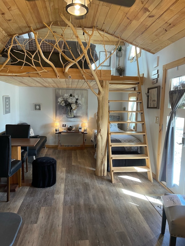 A cozy room with a wooden ceiling, a loft bed, a dining area, and a staircase.