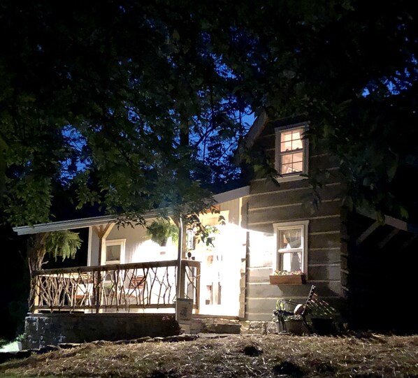 A rustic log cabin with a porch and a small deck, surrounded by trees.