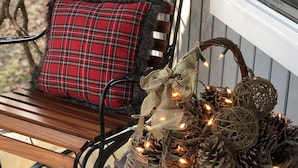 A wooden bench with a red plaid cushion and a small Christmas tree decoration on a porch. - Cedar Twig Cabin: Serene and cozy (Mt. Juliet)
