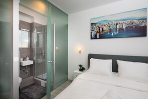 Habitación de hotel moderna con ducha, lavabo y cama con ropa blanca.