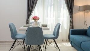 Et spiseområde med et bord dækket til to personer, to blå stole, en vase med blomster og en lampe på et sofabord.