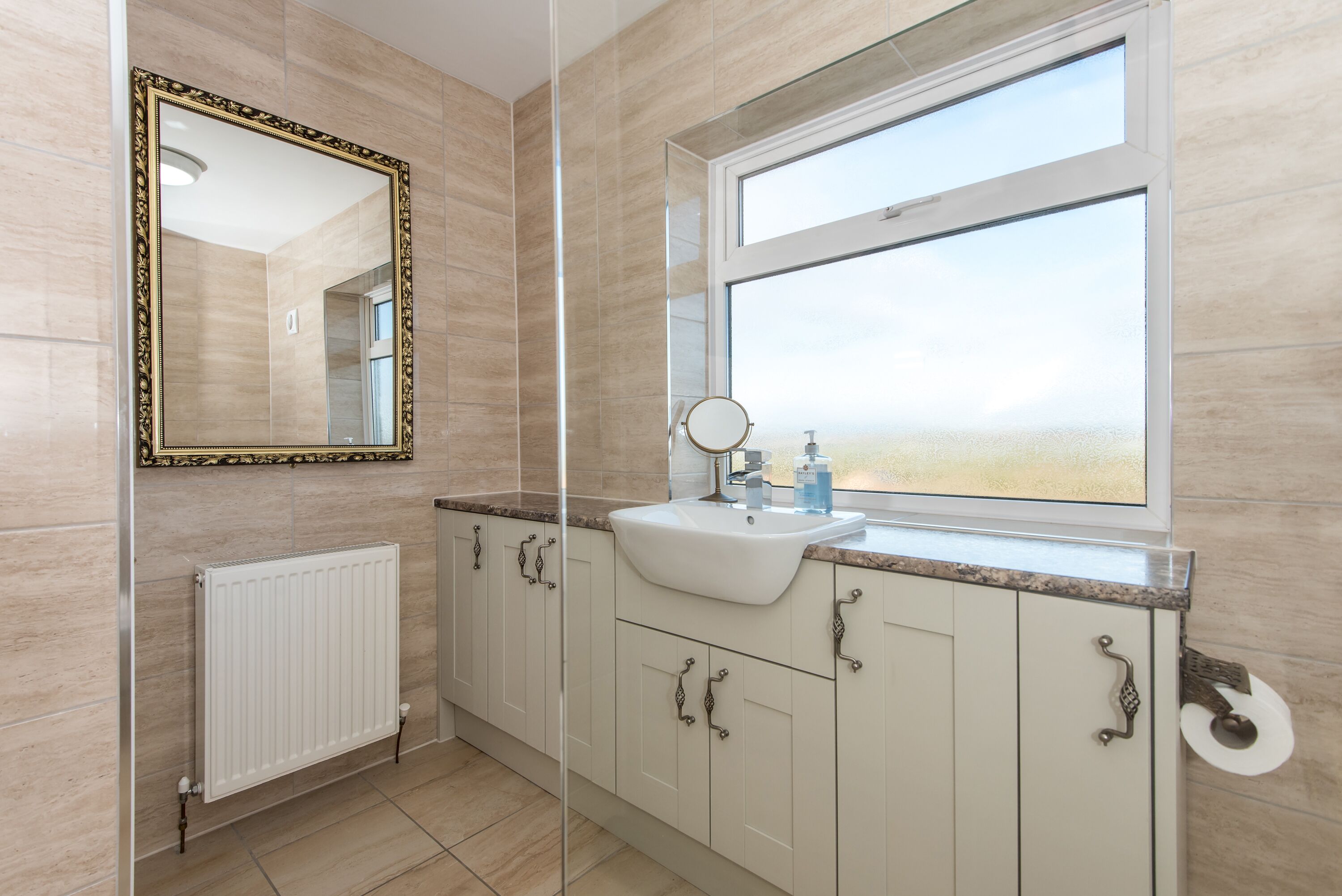 A bathroom with a large mirror, a window, a sink, and cabinets.
