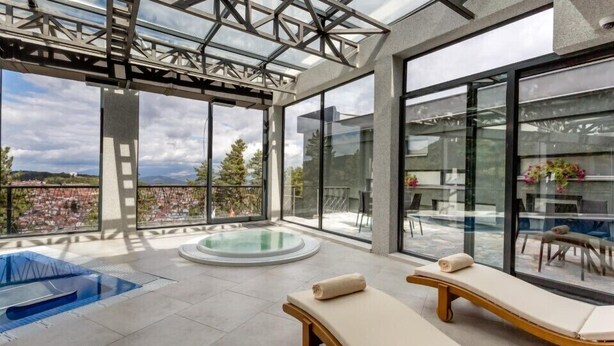 A modern rooftop terrace with a glass-enclosed pool, lounge chairs, and a clear view of the cityscape. - Panorama Hotel & Spa (Krusevo)