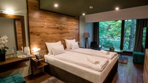 A modern bedroom with a large bed, a wooden accent wall, a bedside table with a lamp, and a view of the outdoors. - Panorama Hotel & Spa (Krusevo)