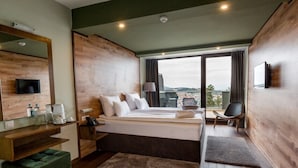 A modern hotel room with a large bed, a desk with a chair, a TV, and a city view. - Panorama Hotel & Spa (Krusevo)