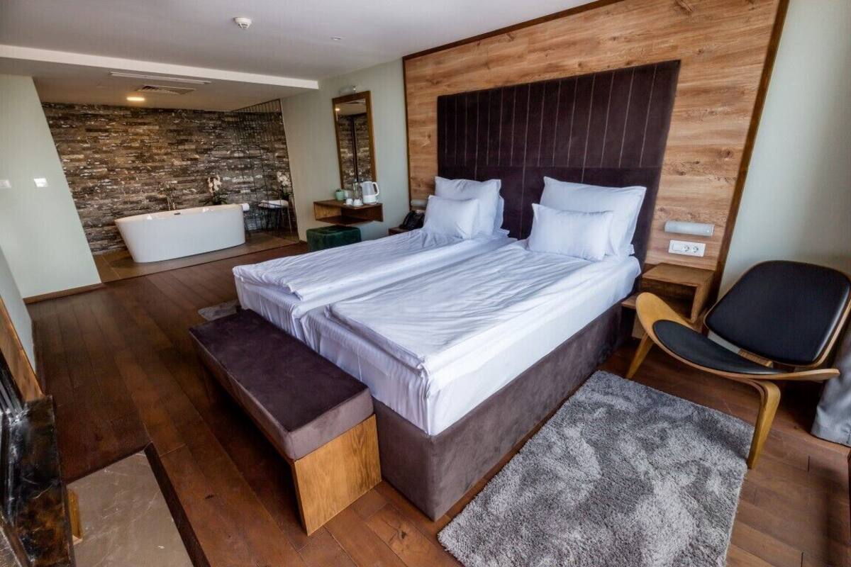 A modern bedroom with a large bed, a bench, a chair, and a bathtub.