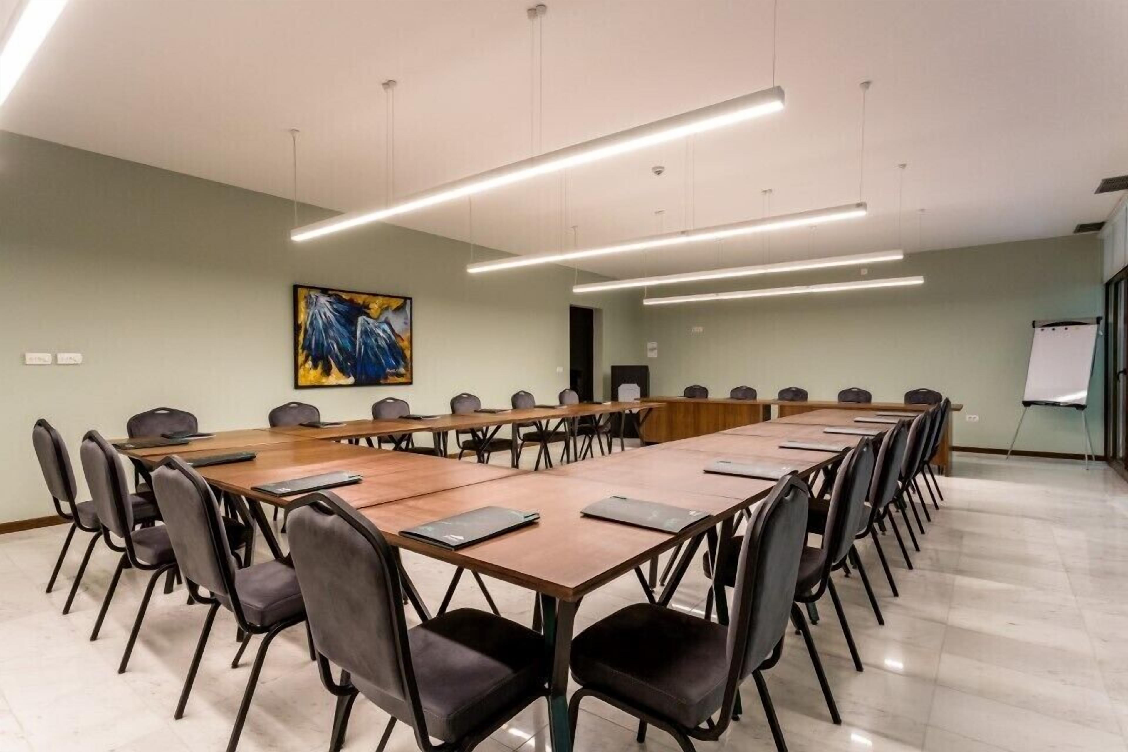 Een vergaderruimte met een lange tafel, stoelen en verlichtingsarmaturen.