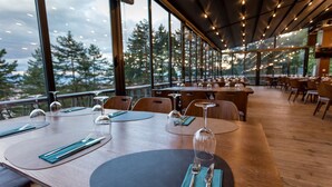 A restaurant with tables set for dining, large windows, and a view of trees. - Panorama Hotel & Spa (Krusevo)