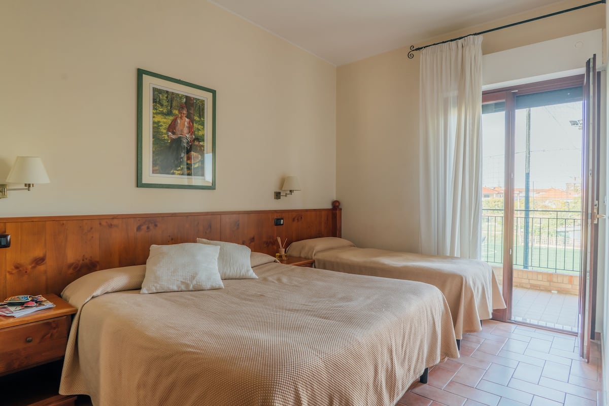 A hotel room with two beds, a wooden headboard, a painting on the wall, and a balcony with a view.