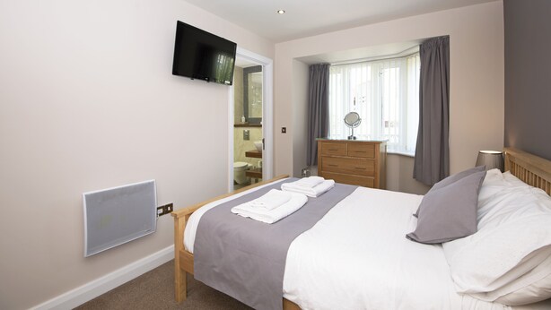A modern bedroom with a bed, a flat-screen TV mounted on the wall, a dresser, and a window with curtains. - Clements Wharf (Durham)