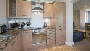 A modern kitchen with built-in appliances, a granite countertop, and wooden cabinetry. - Clements Wharf (Durham)
