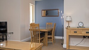 A room with a wooden dining table, two chairs, a TV, a desk with a lamp, and a clock. - Clements Wharf (Durham)
