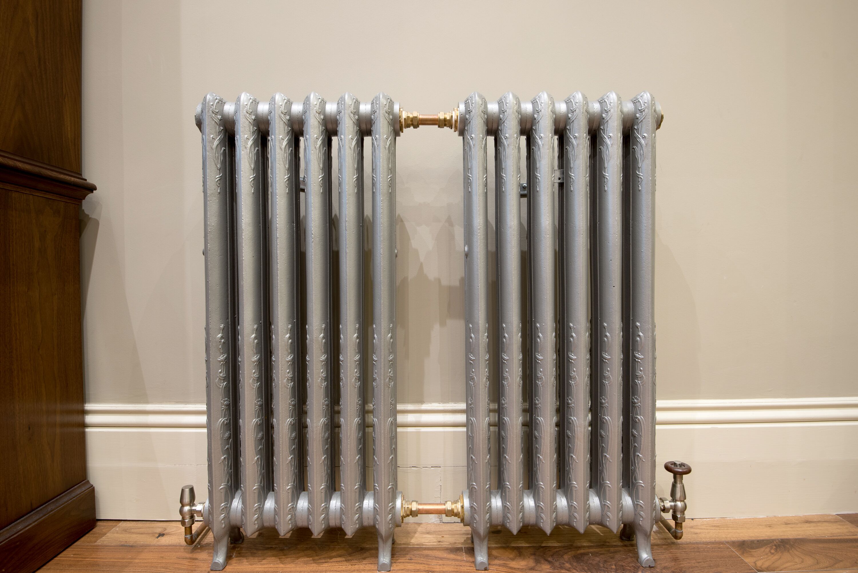 A radiator with intricate designs, positioned against a plain wall.