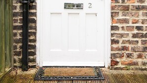 A white door with a number plate, set in a brick wall with a black pipe and a green gate to the left. - Apartment 2 The Grove (Durham)