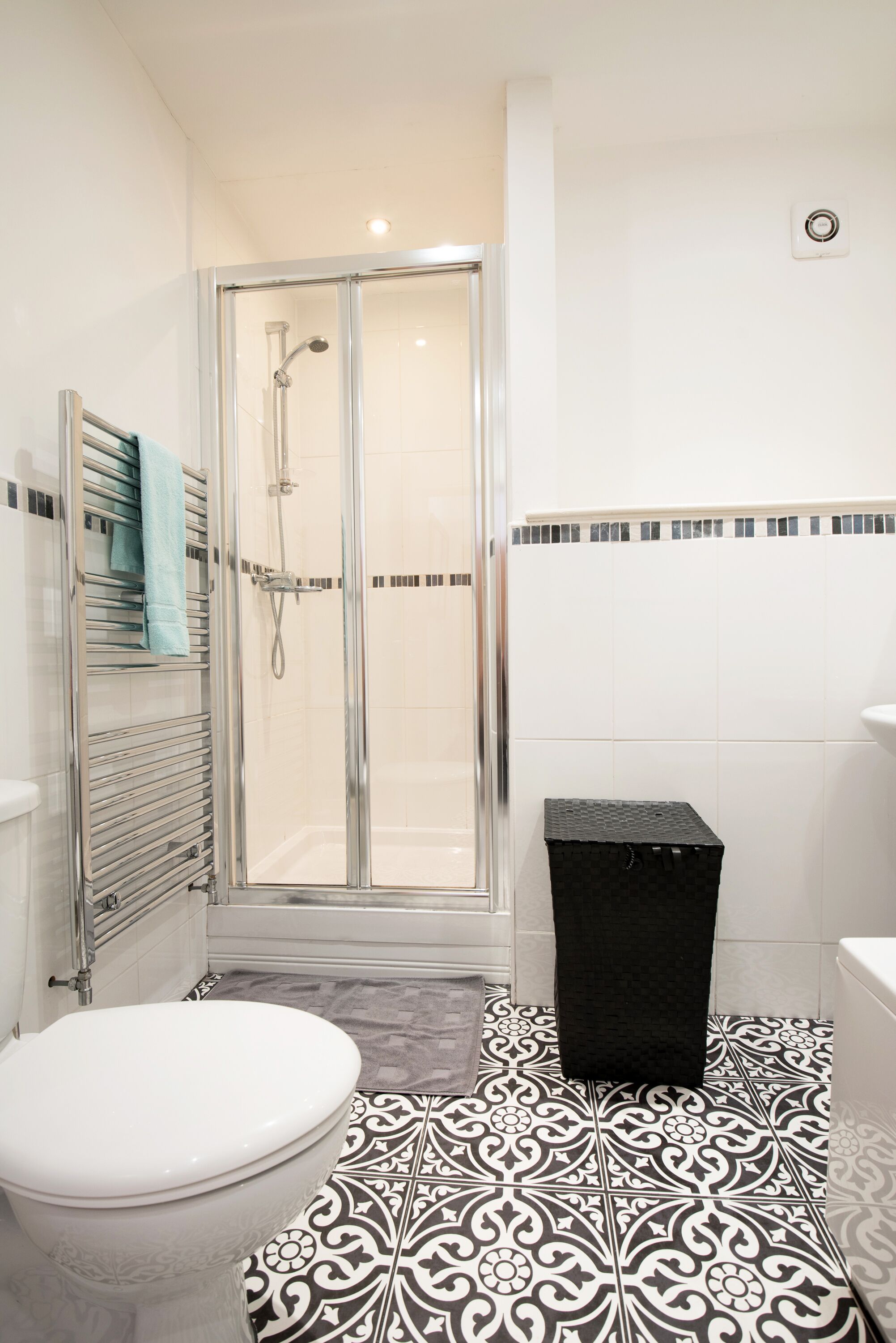 A bathroom with a shower, toilet, and a black trash bin.