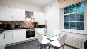 A modern kitchen with white cabinets, a glass table, and white chairs. - Apartment 2 The Grove (Durham)