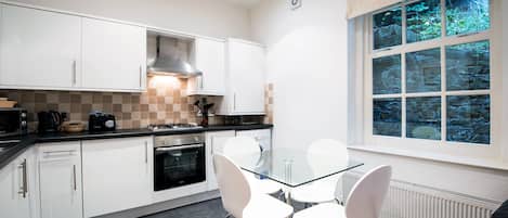 A modern kitchen with white cabinets, a glass table, and white chairs.