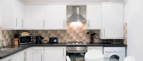 A modern kitchen with white cabinets, a gas stove, a microwave, and a dishwasher.